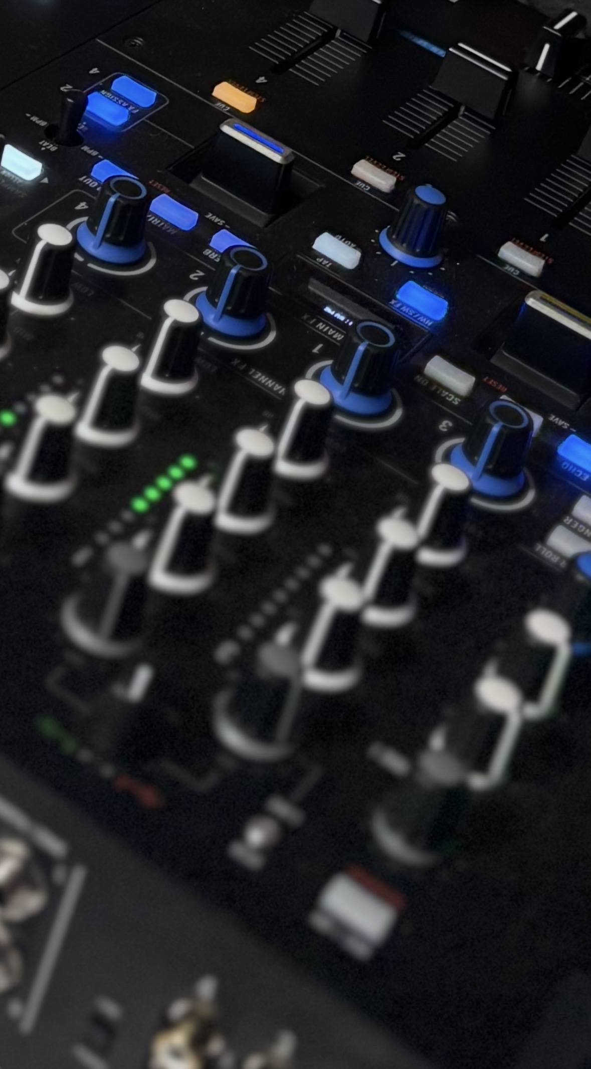 Close-up of a DJ mixing board with illuminated channel faders and controls